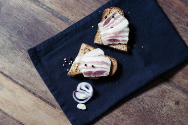 Ahşap masadaki masa örtüsünün üzerinde domuz yağlı ve siyah ekmekli sandviç.