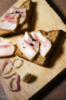 Ahşap masadaki masa örtüsünün üzerinde domuz yağlı ve siyah ekmekli sandviç.