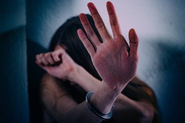 Genç bir kadın şiddete maruz kalıyor, yere oturuyor, ellerini kelepçeleyerek yüzünü kapatıyor. Elleri damarlar ve yaralar, bacakları bir iple bağlanmış. Travma sonrası stres bozukluğu.