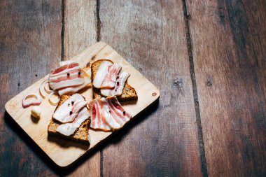 Ahşap masadaki masa örtüsünün üzerinde domuz yağlı ve siyah ekmekli sandviç.