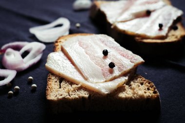 Ahşap masadaki masa örtüsünün üzerinde domuz yağlı ve siyah ekmekli sandviç.