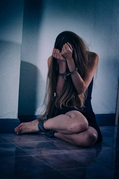 Genç bir kadın şiddete maruz kalıyor, yere oturuyor, ellerini kelepçeleyerek yüzünü kapatıyor. Elleri damarlar ve yaralar, bacakları bir iple bağlanmış. Travma sonrası stres bozukluğu.