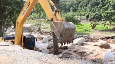 Chiang Rai / Tayland - 20 Ağustos 2018, sel sonrası yollar rehabilitasyonu. Sarı kazıcı Komatsu nehirde duruyor ve kendini yere bırakıyor. Yolun sonu..