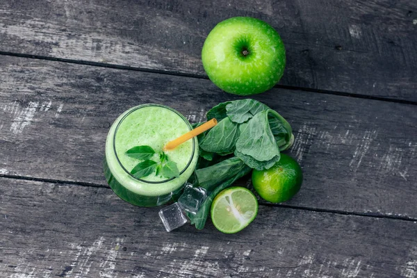 Green apple smoothie in glass and kale leaves on rustic wooden table. Summer Detox shake background