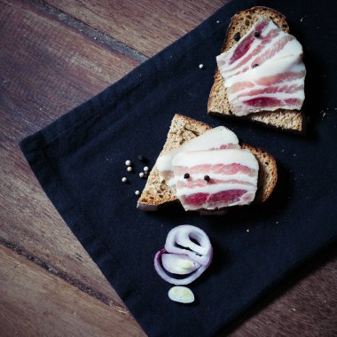 Ahşap masadaki masa örtüsünün üzerinde domuz yağlı ve siyah ekmekli sandviç.