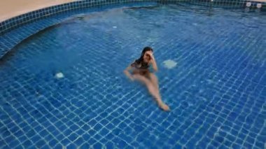 Açık mavi yüzme havuzunda yüzen genç bir kadın. Açık hava aktiviteleri. Sağlıklı bir yaşam tarzı. Üst görüntü video 4k.