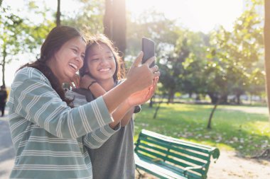 Asyalı anne ve kızı parkta selfie çekiyor.