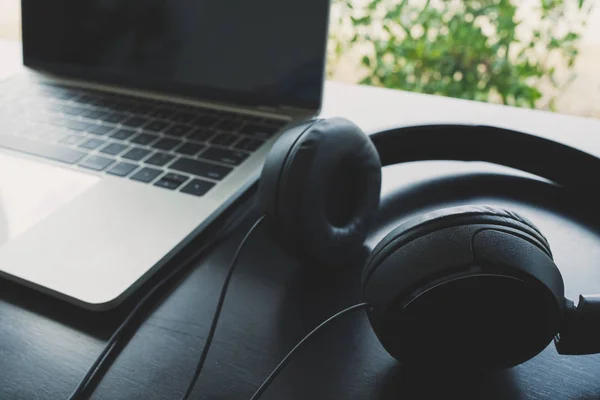 Siyah ahşap bir masaya yerleştirilen siyah kulaklıklar ve dizüstü bilgisayarlar