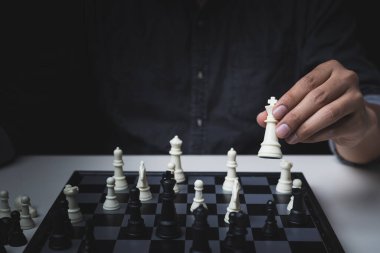 Siyah arka plan, iş rekabeti konsepti üzerine siyah gömlek giyen beyaz satrançlı bir adamın el görüntüsü