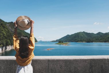 Bir kadın turistin arkası ve elinde şapka Arka planda nehirler ve dağ var