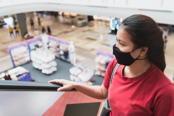 アジアの女性は医療用マスクを着用し ショッピングモールでエスカレーターを使用しています ストック写真