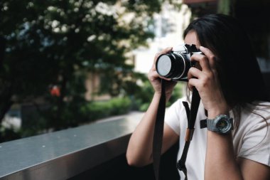 Asyalı bir kadın kahve dükkanında oturmuş film kamerasıyla fotoğraf çekiyor.