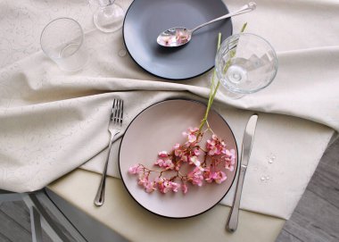 Bej masa örtüsü ve tabağı olan bir yemek masası. Begonya çiçekleriyle dolu bir masa. çatal bıçak görünümlü bir masanın fotoğrafı.