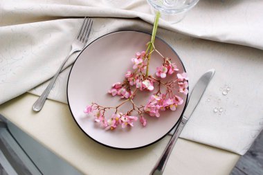 Bej masa örtüsü ve tabağı olan bir yemek masası. Begonya çiçekleriyle dolu bir masa. çatal bıçak görünümlü bir masanın fotoğrafı.