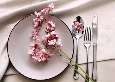 Tabak ve çatal bıçak seti masanın üstünde. Masa olarak pembe begonya çiçekleri. İçsel detaylar, şenlikli masa ayarları.