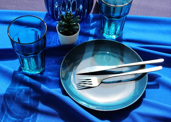 mavi arka plan. Masa mavili ve çatal bıçaklı. Masadaki tabak ve çatal bıçak seti gün ışığında. Yukarıdan bak. iç ayrıntılar.