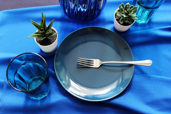 Doymuş mavi. Yemek odasının içerisi, çatal bıçaklı sofra takımı ve çanak çömlek takımı. Masanın üzerinde mavi bir masa örtüsü ve mavi tabaklar var..