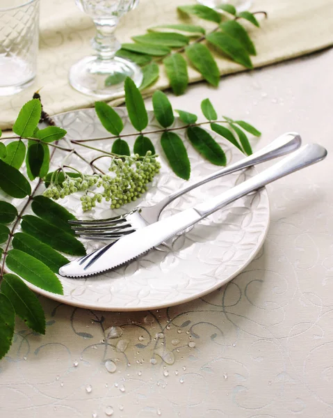 Bej seramik bir tabakta çatal ve bıçak seti, dağ külünden yeşil bir dekoru olan bir masanın üzerinde, yakın plan. Festival masası dekoru, ayrıntılar.