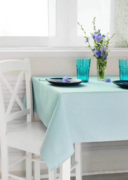 Masada mavi bir masa örtüsü ve parlak bir odada pencerenin yanında bulaşıklar. romantik yemek masası detayları ayarlıyor.