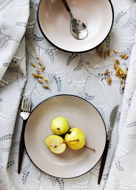 Masa takımı. Tabaklar masada, armut ve çatal bıçak takımı var..