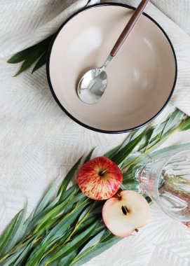 Masanın üzerinde yeşil yapraklar ve kırmızı elmalardan oluşan bir kaşık ve dekorasyonla seramik kalın tabaklar servis ediliyor. Yukarıdan görünüşü.