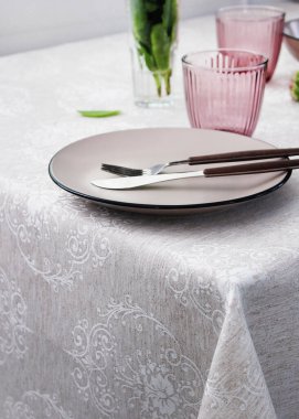 Masa ayarı. Tabaklar masanın yan tarafındaki yakın çekim görüntüsünde. Gri masa örtüsü ve bej tabak ve çatal bıçak takımı..