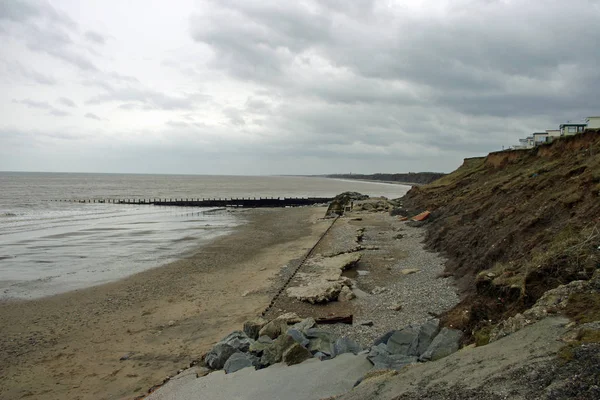 遊歩道と海防御回数が崩れ 下にあるビーチへの落ち イギリスの東海岸の侵食を示します 崖とキャラバンの背景が海と灰色の空と崖の端に近い — ストック写真