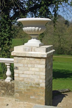Süs jardiniere bir tuğla ayağı üzerinde eski bir duvarına bitişik ve korkuluk ışık gri renkli tuğla inşa. Çimenler, ağaçlar ve arka planda mavi gökyüzü.