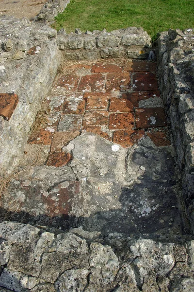 粘土は 英国で出土したローマ時代のヴィラの床のタイルします 壁のベースが表示されます タイルの地衣類 バック グラウンドで草します — ストック写真