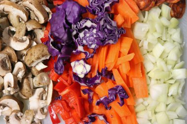 Stir fry beyaz plastik tahtası için doğranmış malzemeler. Soğan, havuç, mantar, biber, kırmızı lahana ve chorizo gıda içerir.