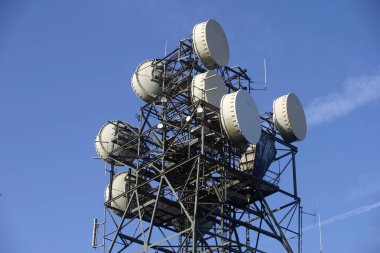 Antenler ve yemekleri ile metal telekomünikasyon mast. Arka plan beyaz uçak contrails ile mavi gökyüzünde.