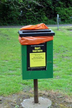 Yeşil köpek çöp kutusu metal bir yazı üzerine beton Danışma etiket, siyah kapak, bir turuncu Plastik depo gözü liner ve çim, yol ve ağaçlar bir arka plan ile ön görülen ayarla.