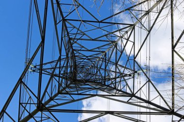 Yüksek gerilim elektrik pilon veya güç iletim kulesi doğrudan altında her bakıldığında kabloları ile. Arka plan beyaz bulutlar ile mavi gökyüzü.