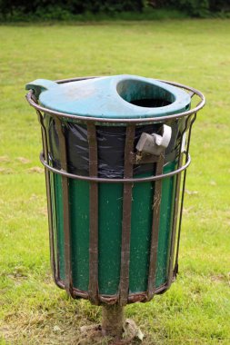 Bir çim çim bir parkta bir siyah plastik depo gözü astar içinde içeren bir metal çerçeve yeşil çöp Kutusu'na çevrili.