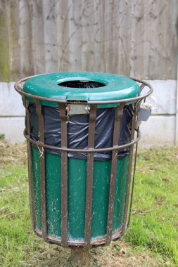 Çim ve arkasında ahşap bir çit ile içinde bir siyah plastik depo gözü astar içeren bir metal çerçeve yeşil çöp Kutusu'na.