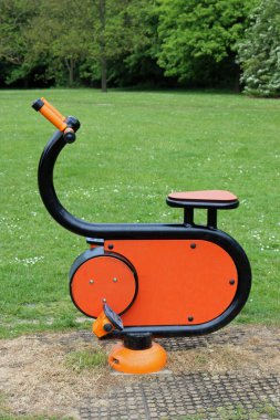 Bir parkta çim çim üzerinde modern parlak turuncu spor salonu ekipman Emanet çalılar ve ağaçlar içinde belgili tanımlık geçmiş ile tabanı etrafında yüzey aşınma ile.