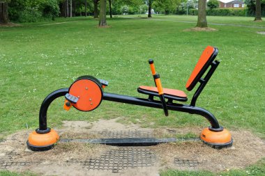 Bir parkta çim çim üzerinde modern parlak turuncu spor salonu ekipman emniyet evleri, çalılar ve ağaçlar içinde belgili tanımlık geçmiş ile tabanı etrafında yüzey üzerinde aşınma ile.