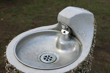 Metal park çeşme ile bir çakıl taşı kesikli dış beton bir kaide üzerinde kase ile.