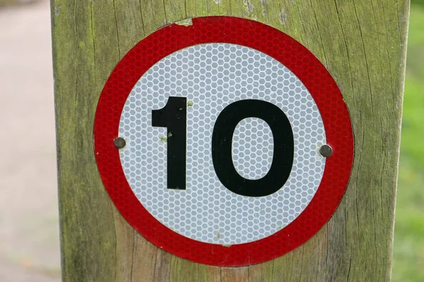 10 mph speed restriction vehicle warning sign on a wooden post background in a park with grass to the right and road to the left.