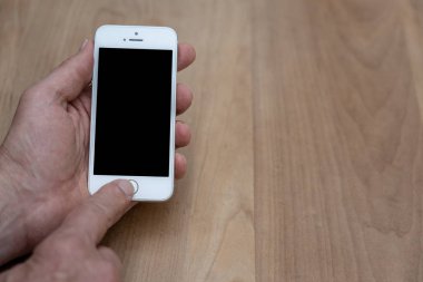 İnsan eli bir kahverengi ahşap arka plan üzerinde beyaz bir akıllı telefon tutarak. El ev düğmesi çalışıyor