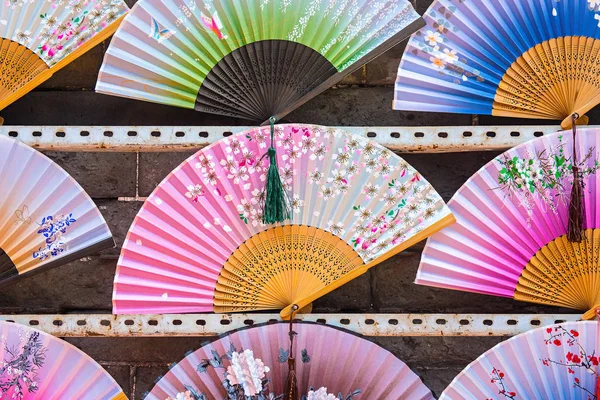 Different colors of hand fans are displayed for sale. People usually use them in warm and tropical areas to give themselves a sense of coolness