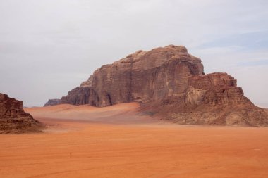 Ürdün 'deki Wadi Rum çölünde bulutlu bir gökyüzünün altında kırmızı kum ve kayalar..