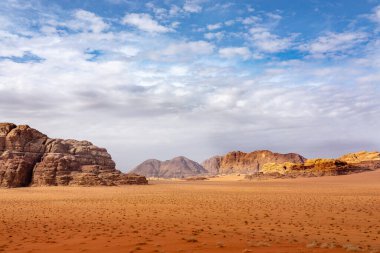 Ürdün 'deki Wadi Rum çölünde bulutlu bir gökyüzünün altında kırmızı kum ve kayalar..