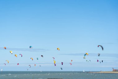 Uçurtma sörfçülerinin büyük bir kısmı mavi gökyüzünün altında sporlarını denizde yapıyorlar. Yelkenler parlak renkli.