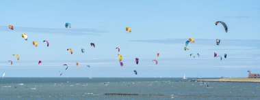 Uçurtma sörfçülerinin büyük bir kısmı mavi gökyüzünün altında sporlarını denizde yapıyorlar. Yelkenler parlak renkli.
