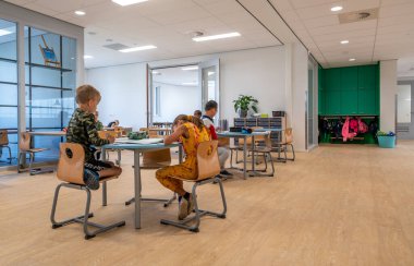 ARNHEM / NETHERLANDS - 28 AĞUSTOS 2020: İlkokuldaki çocuklar grup olarak çalışırlar. Modern bir okul binasındalar.