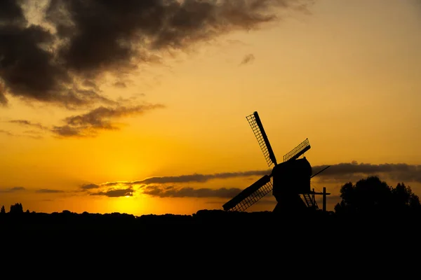 田舎の風景の中で太陽が昇るまたは沈むの赤いオレンジ色の光に対する伝統的なオランダの風車のシルエット — ストック写真