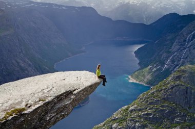 Trolltunga kaya (Troll dil rock) üzerinde oturan ve Norveç dağ manzarası arayan kız