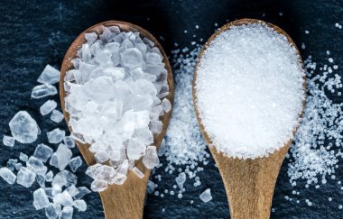 Tuz farklı türleri. Deniz ve mutfak tuz. Siyah arka plan üzerine iki tahta kaşıklar üzerinde Üstten Görünüm