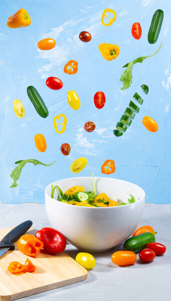 Levitating mixed vegetables on blue background. Magical cucumber, tomato and paprika with white bowl